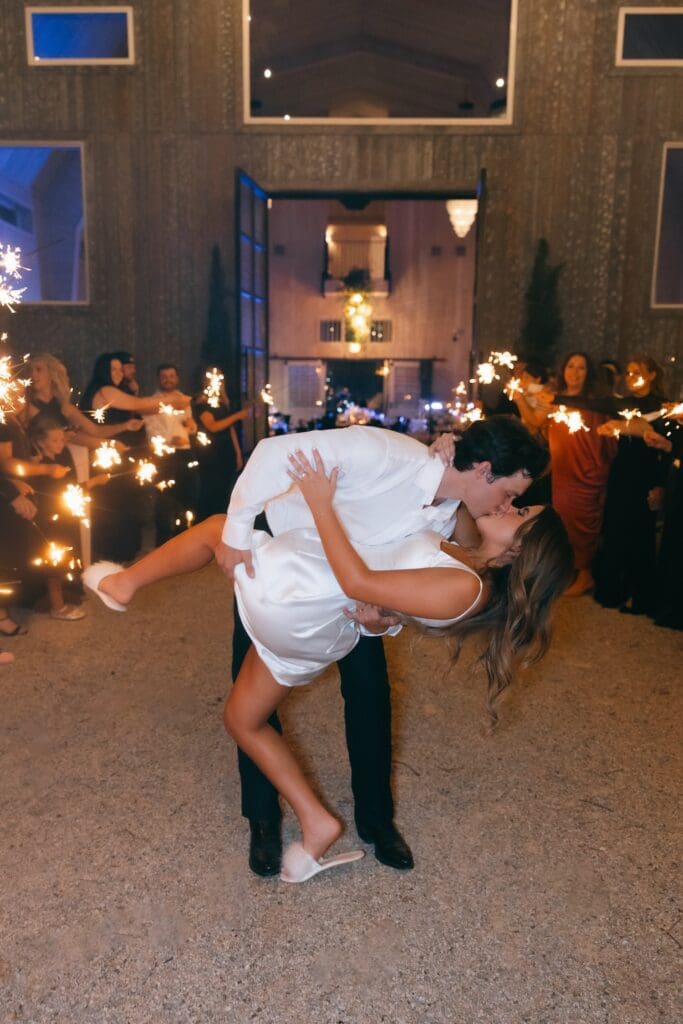 Bride and groom kiss existing their wedding with sparklers in Texas.