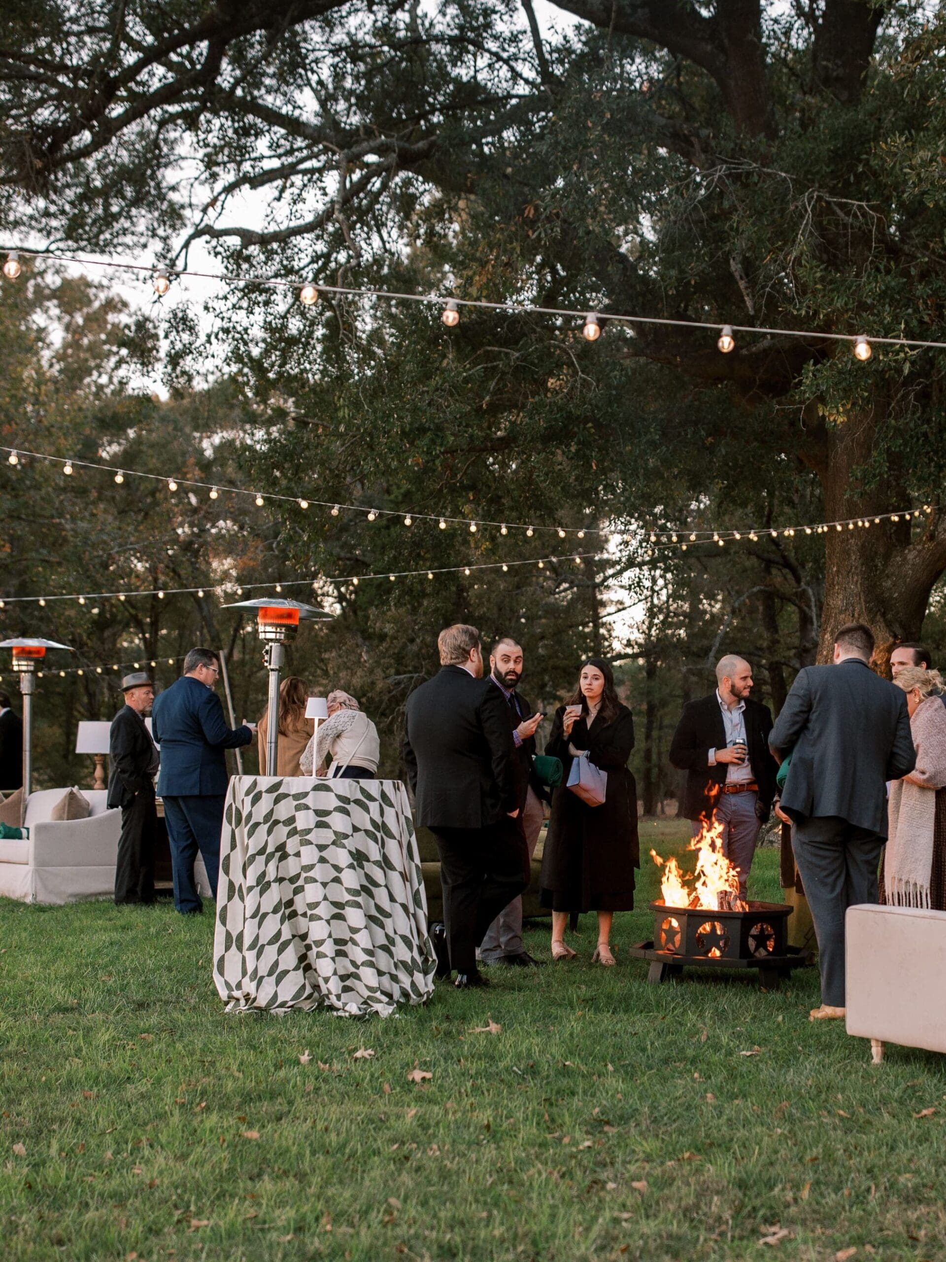 Wedding guests mingle around cozy campfire during a relaxed cocktail hour.