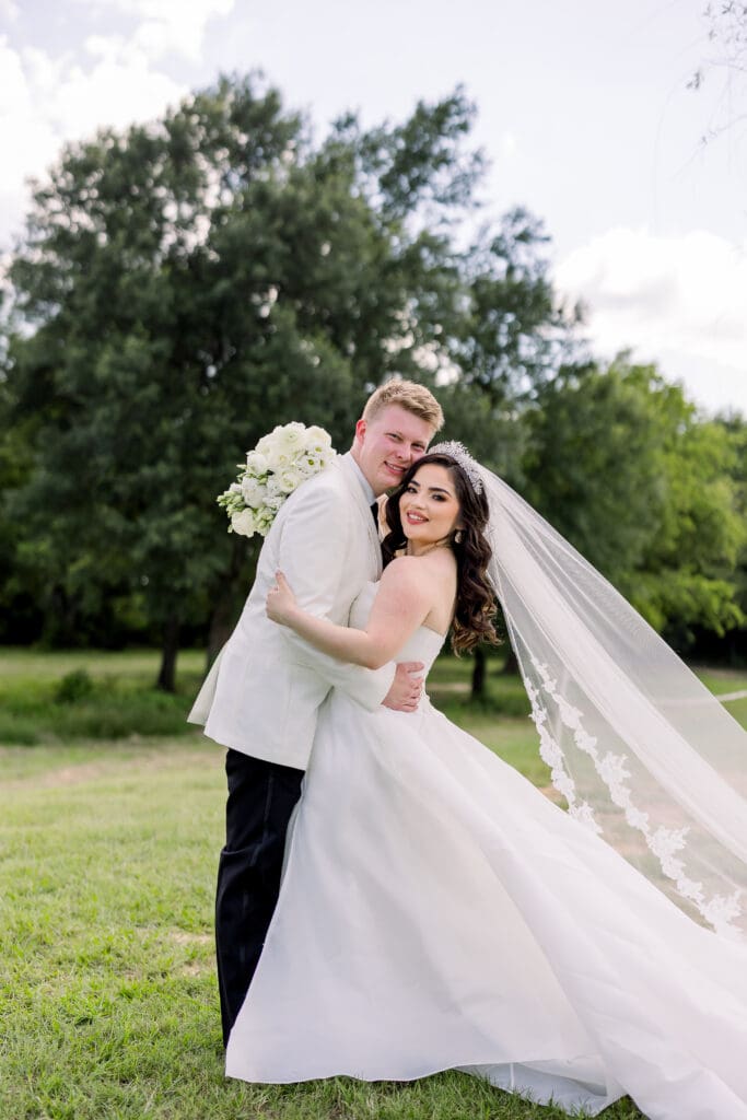 A lovely bride stands with her groom wearing a ballgown, tiara, and long veil.
